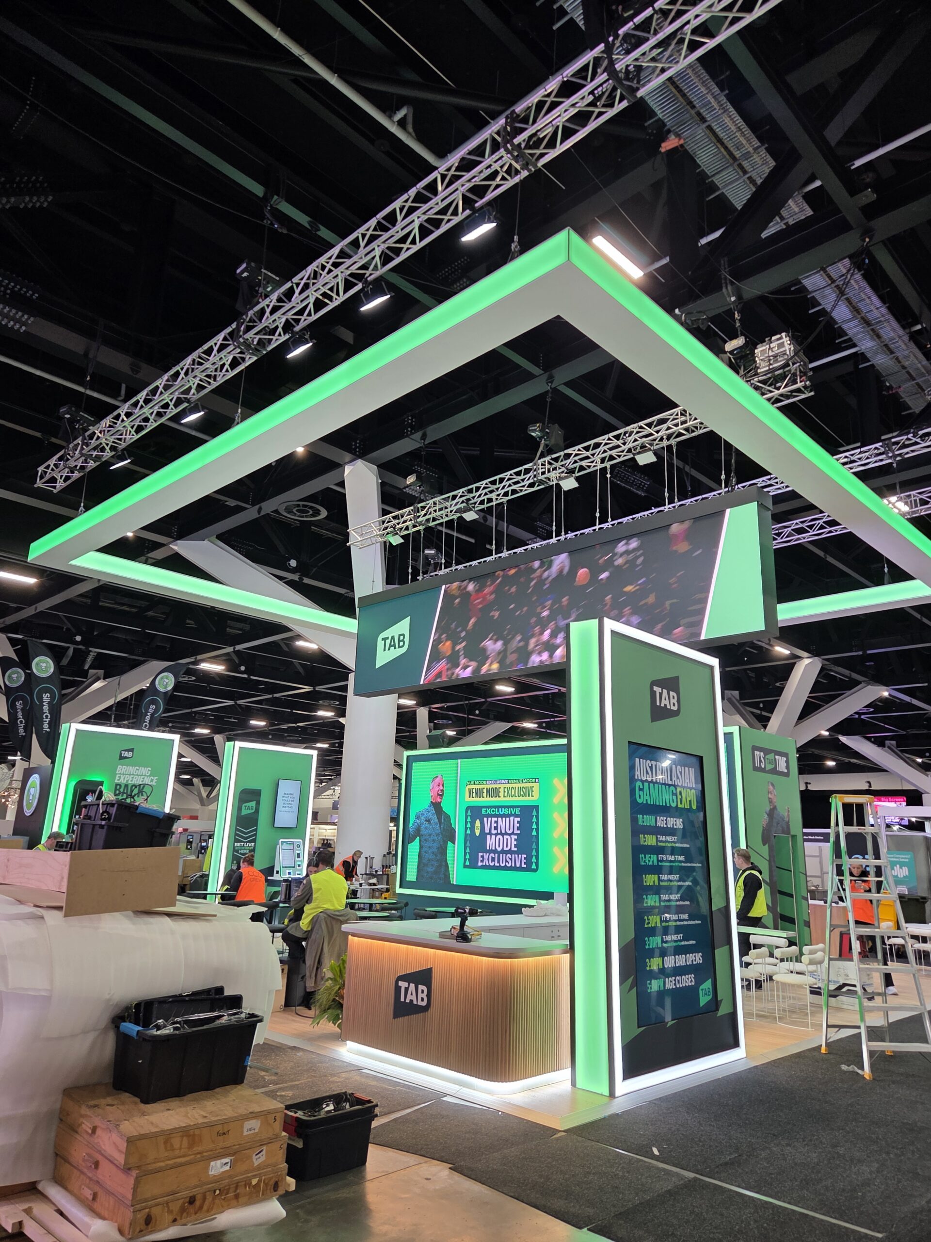 TAB exhibition booth at Australasian Gaming Expo with green lighting and large screens.