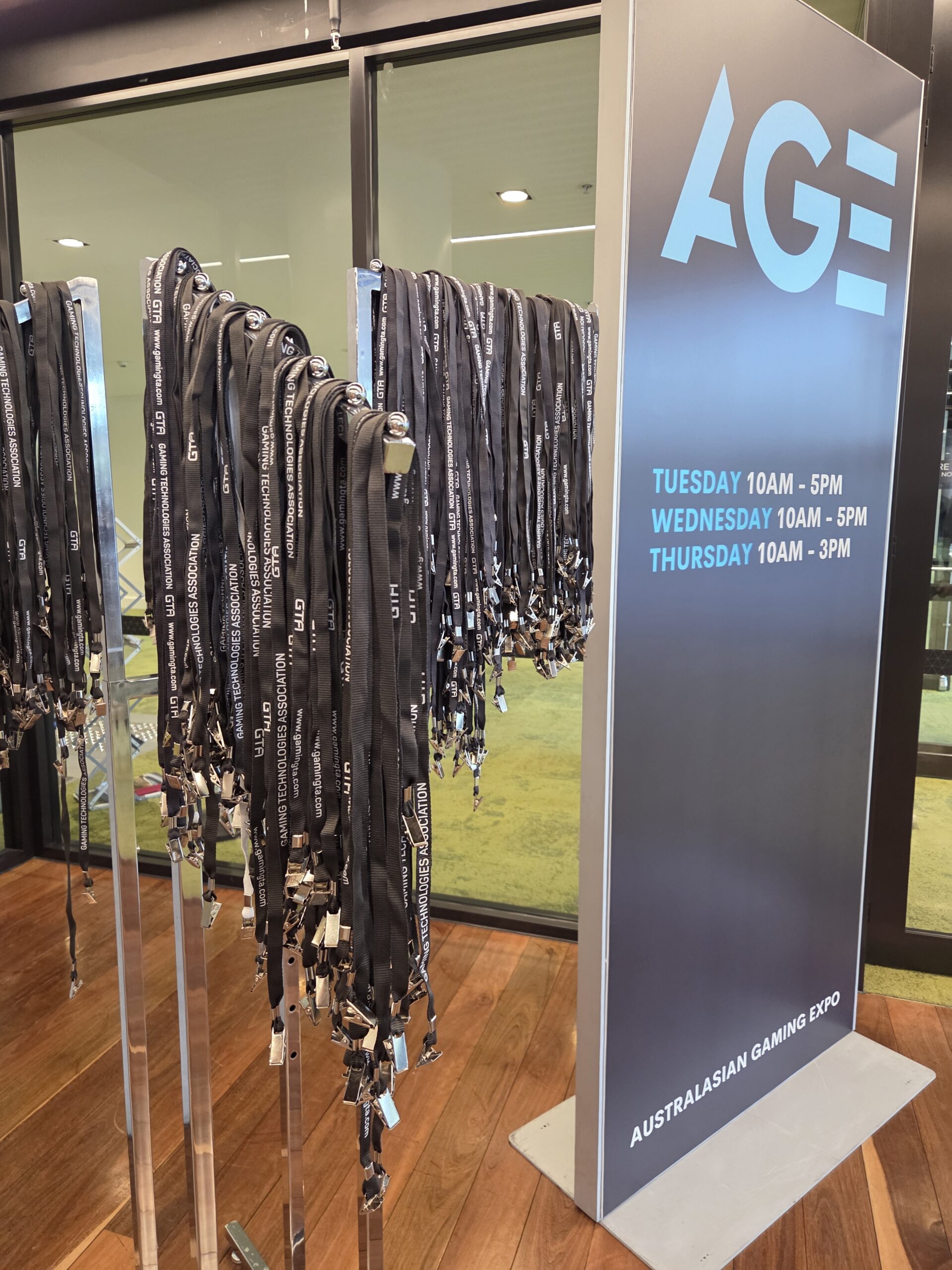 Lanyards on racks beside an Australian Gaming Expo 2025 sign with Day 1 Wrap-Up details displayed.