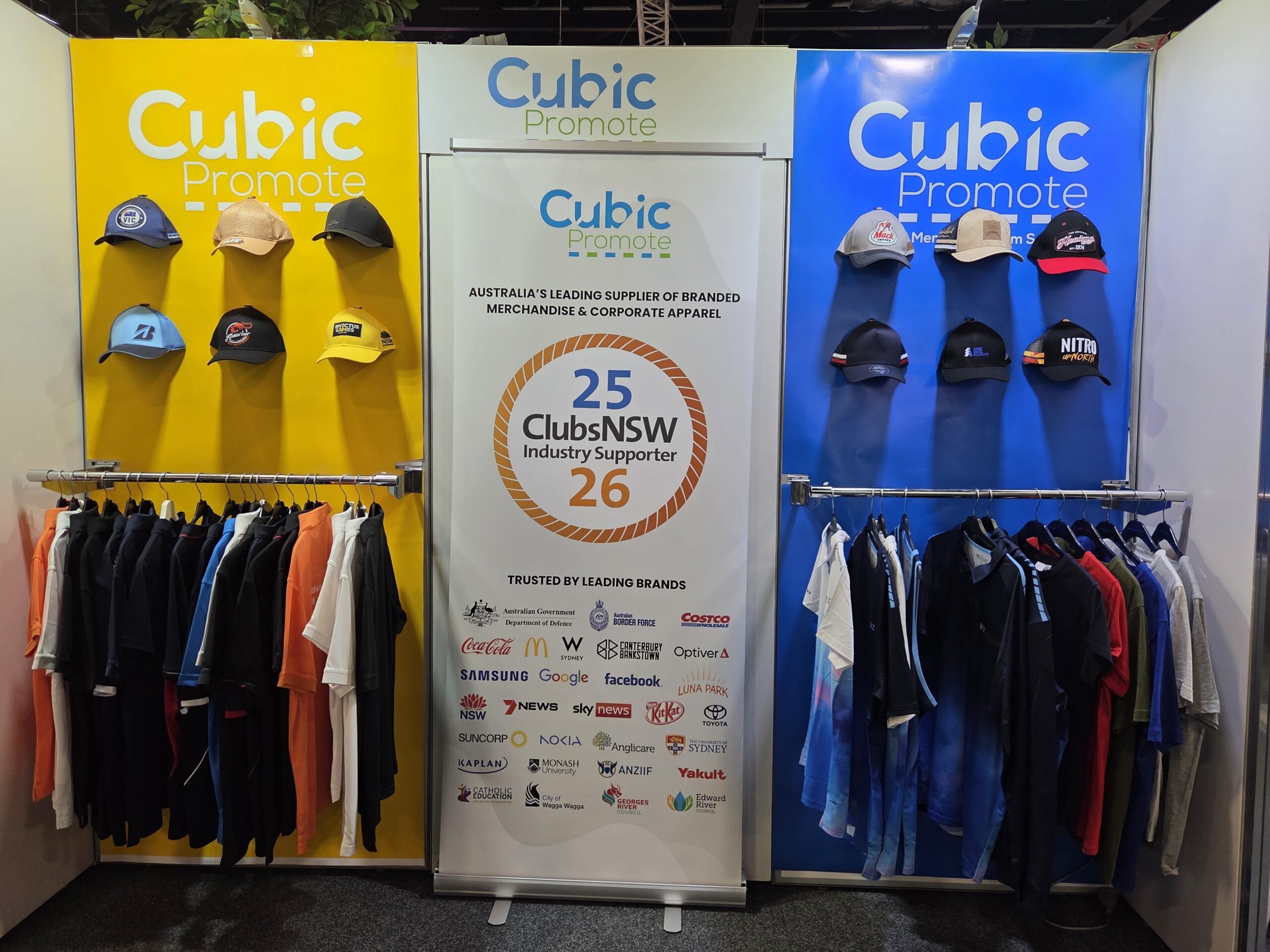 Display booth with hats and shirts, Cubic Promote branding, and a gaming 2025 trusted brands sign.