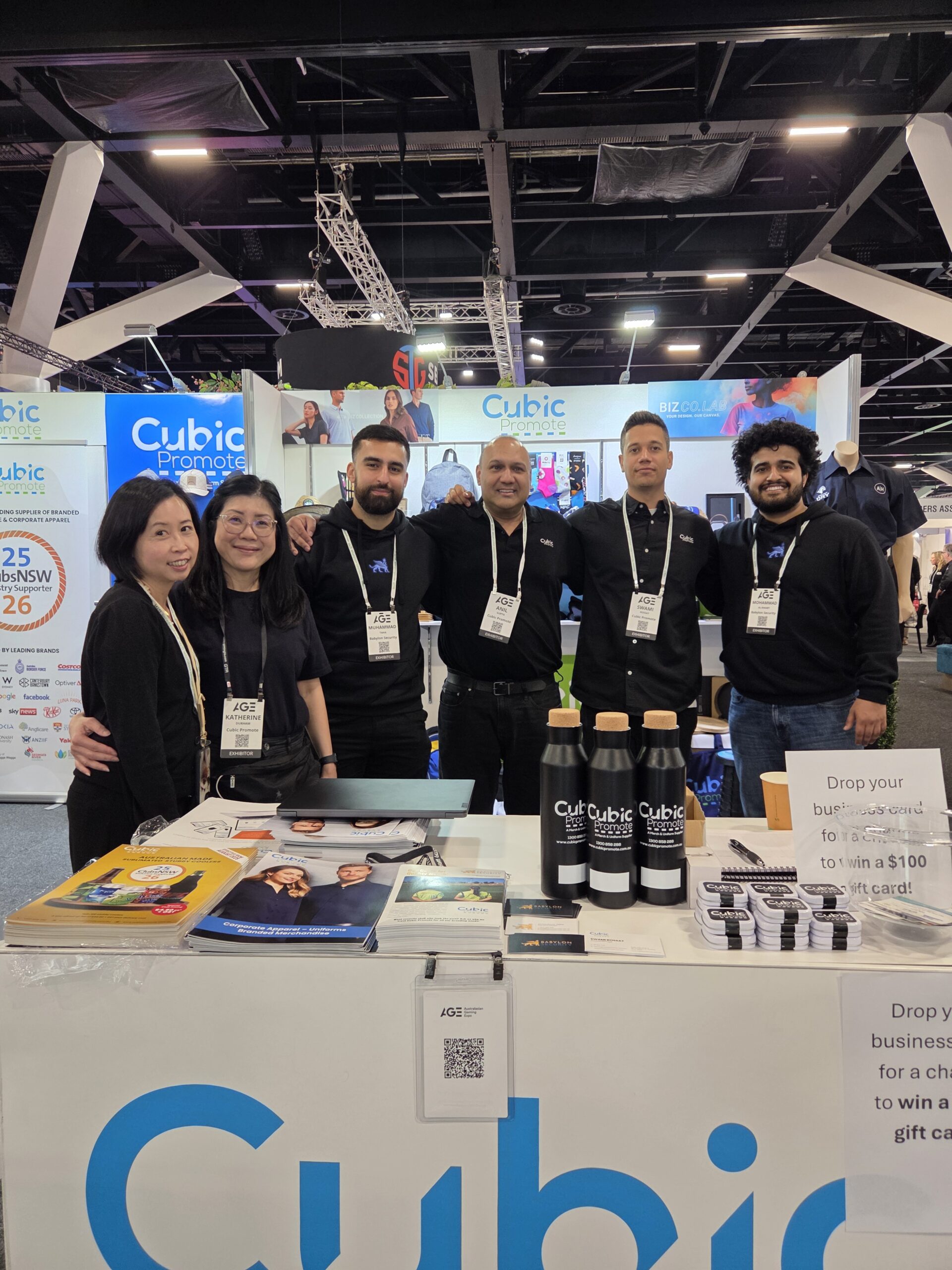 Six people smiling at a gaming 2025 trade show booth with branded items and promo materials.