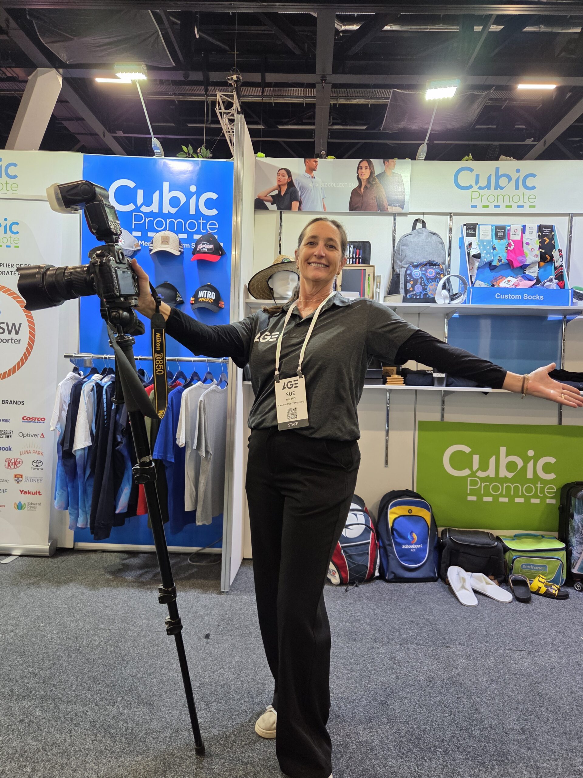 Woman smiling with a camera at the Cubic Promote booth at a gaming 2025 event.