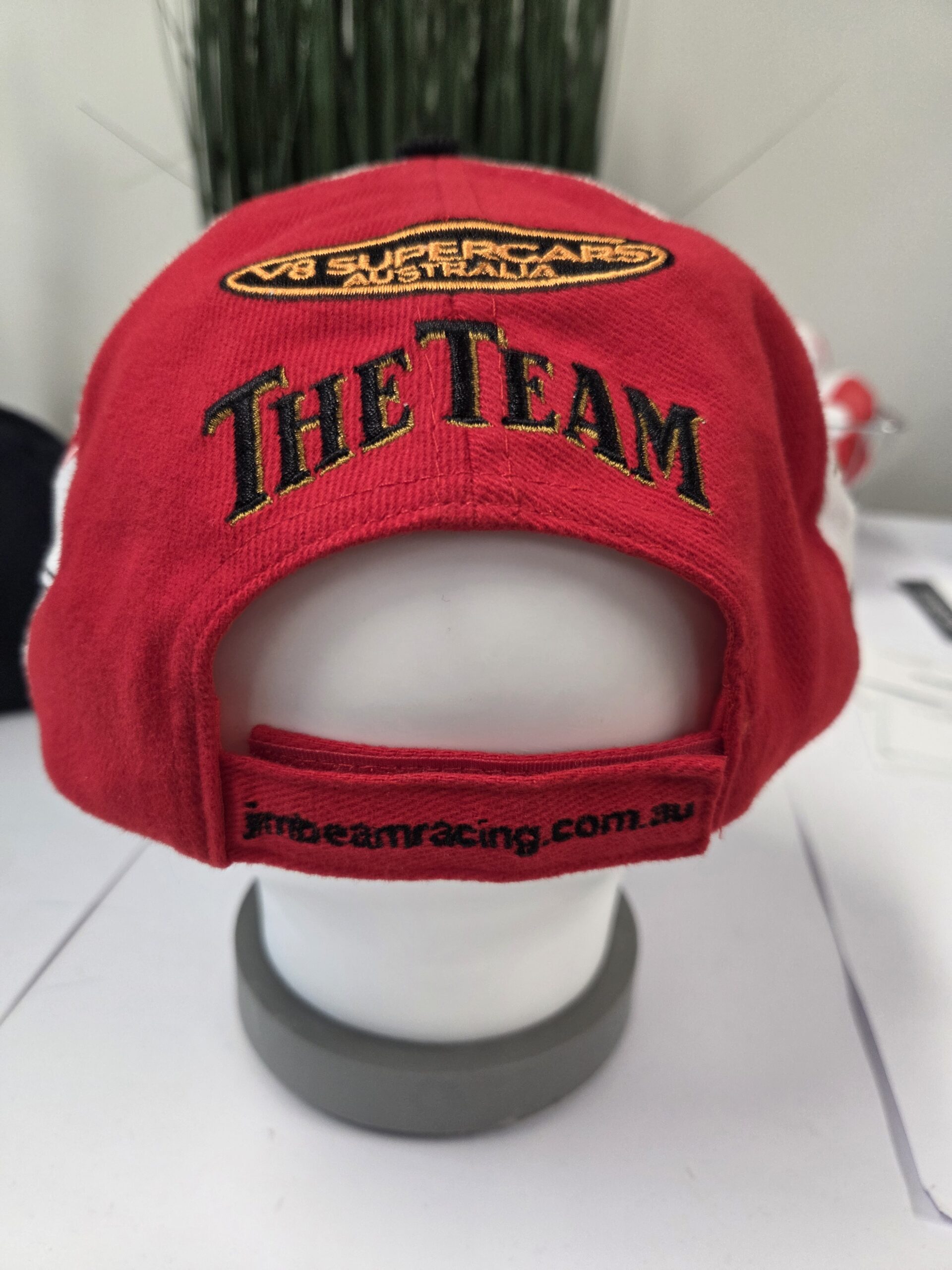 Red branded cap with The Team text, Supercars V8 patch, and adjustable cap closures.