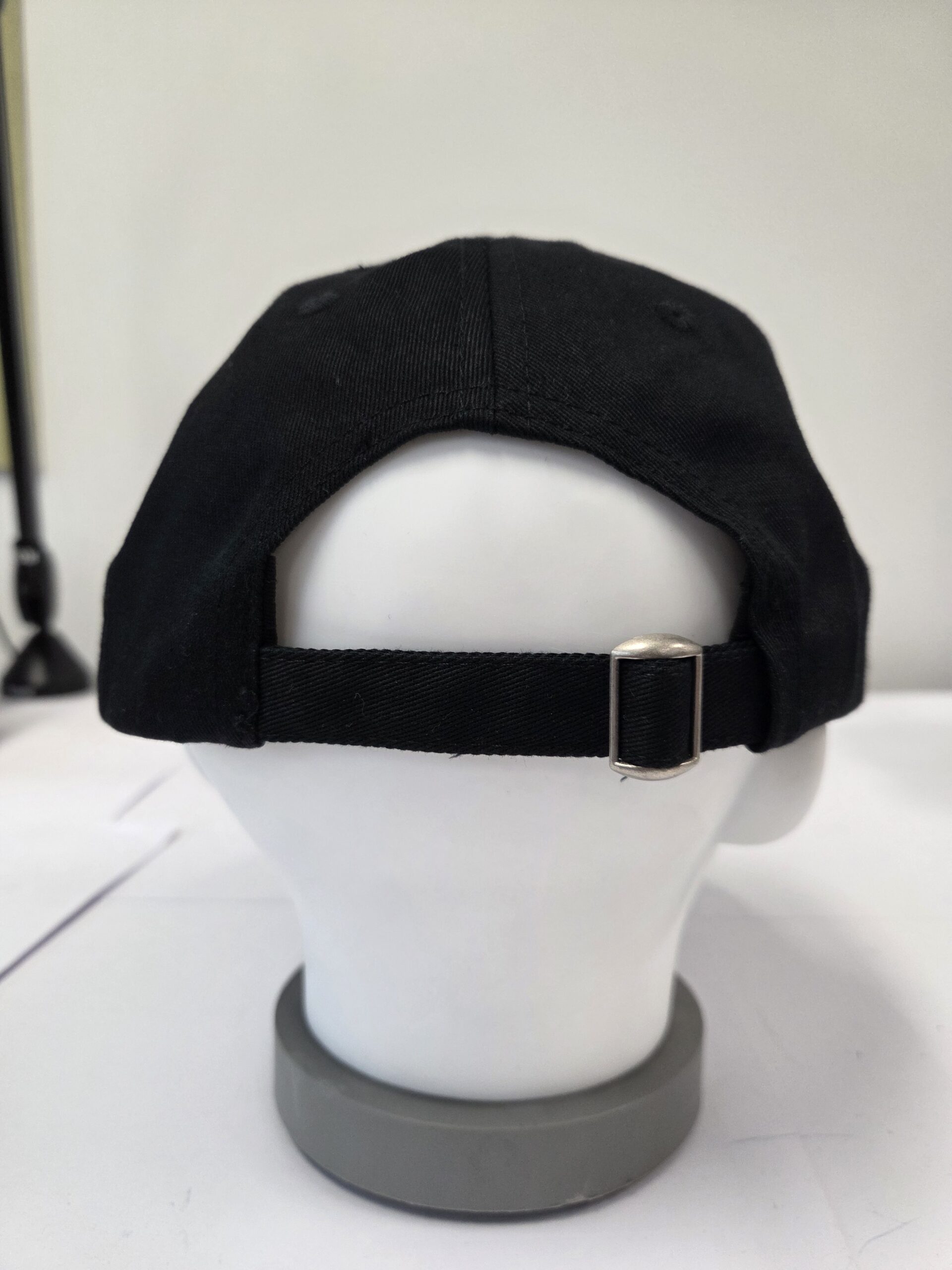 A black baseball cap on a mannequin head, shown from the back with adjustable cap closures.