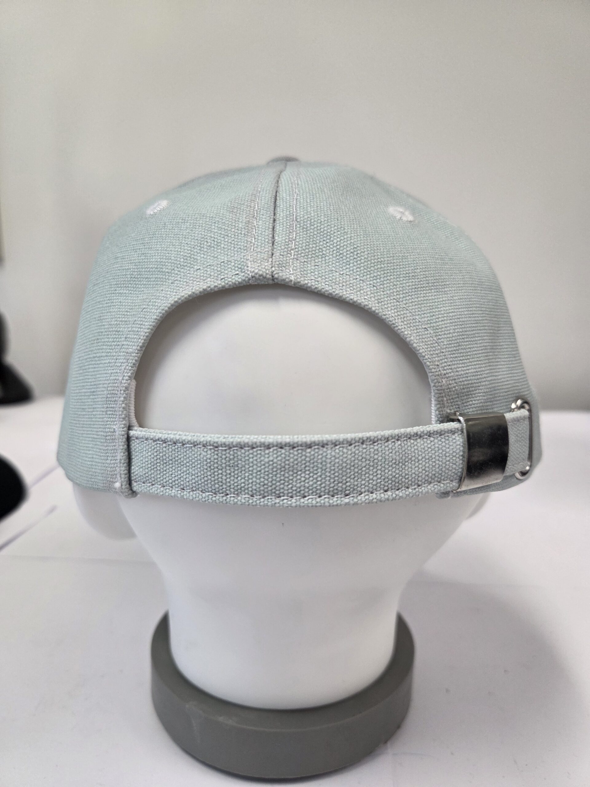 A light gray branded cap with adjustable cap closures on a mannequin head, viewed from the back.