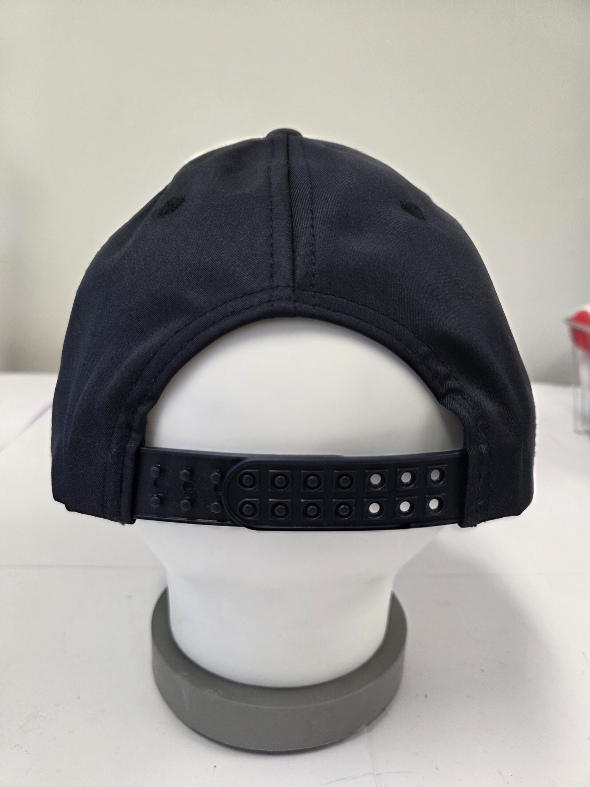 Back view of a black snapback cap with adjustable cap closures on a white mannequin head.