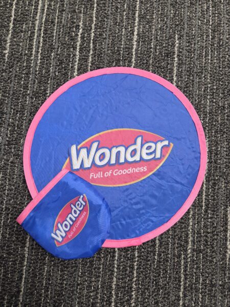 Blue and pink soft promotional frisbee and pouch on a striped carpeted floor.