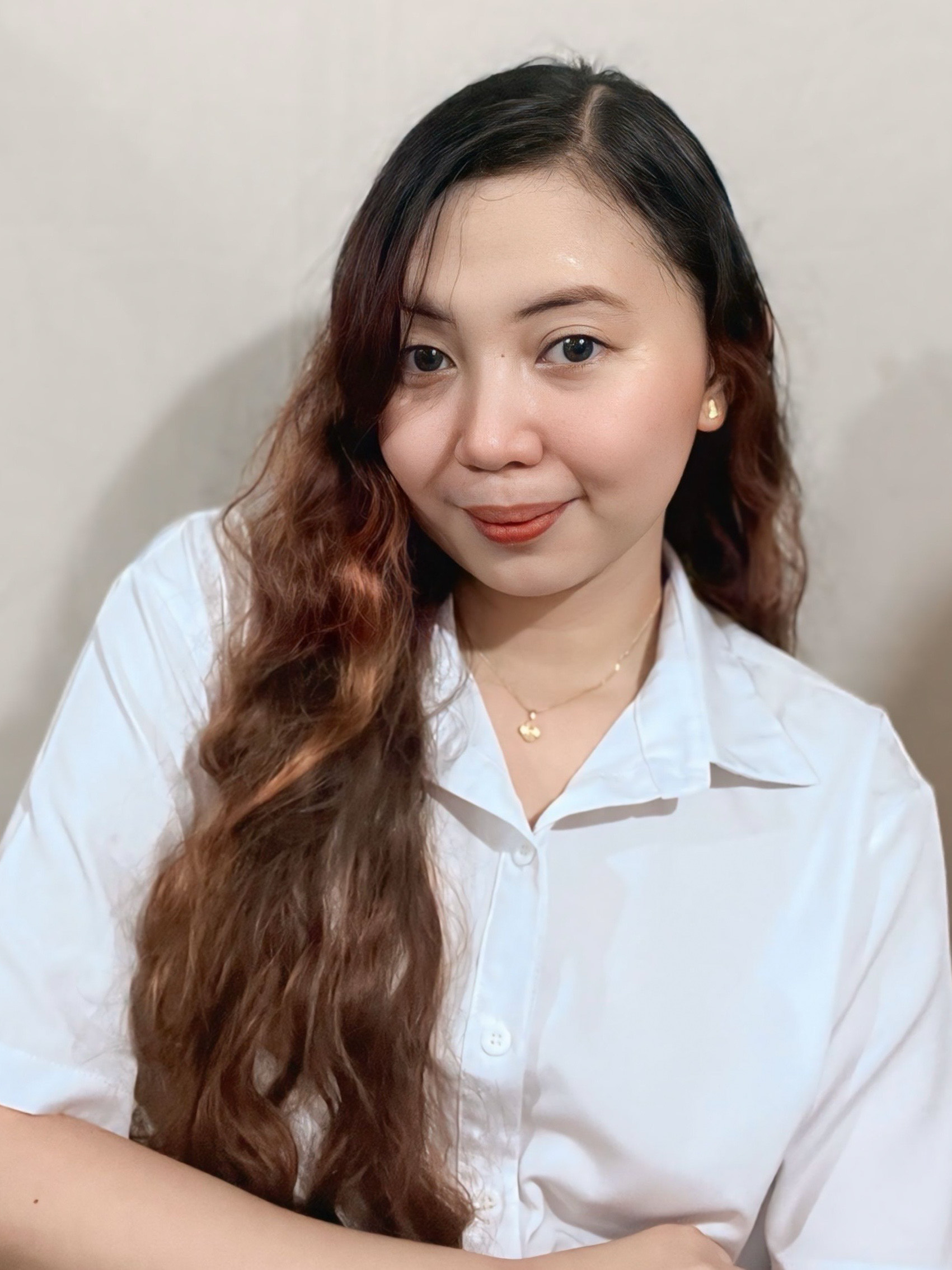 Woman with long wavy hair in a white shirt, smiling, modeling custom merchandise.