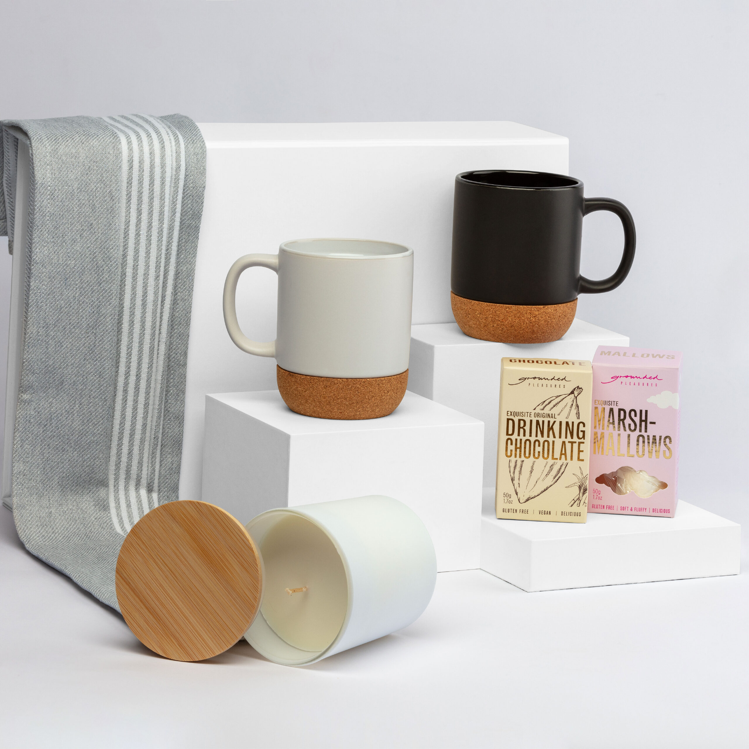 The First Impressions Hampers: 2 mugs, candle, hot chocolate mix & marshmallows on white blocks.