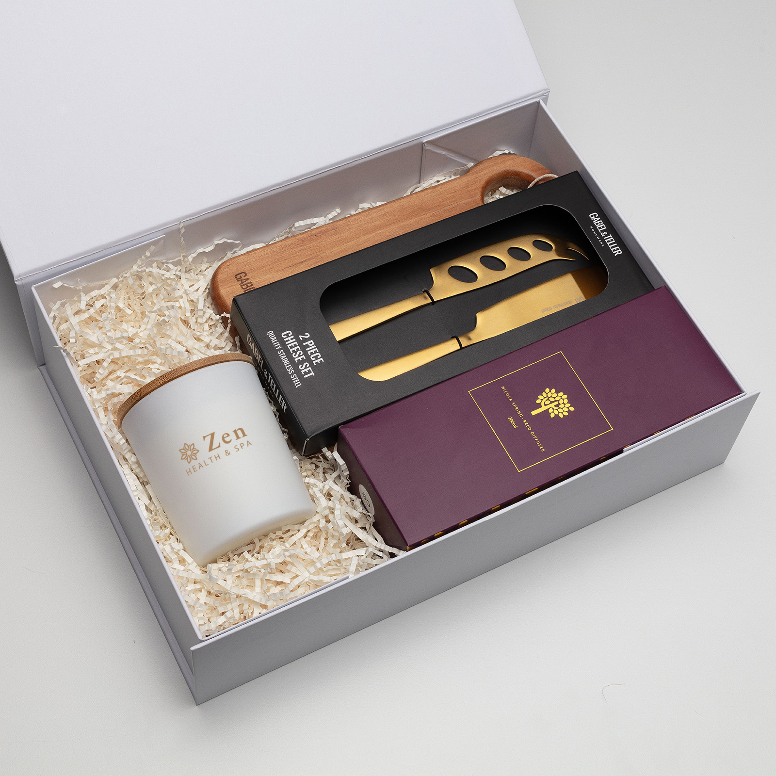 The Curated Host Hampers: Gift box with candle, gold cheese knives, and a purple booklet.