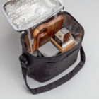 Open black insulated lunch bag from Graze Hampers with a cutting board, cheese, and snacks inside.