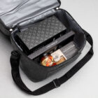 An open black bag with cheese set, crackers, chutney, and The Partnership Graze Packs.