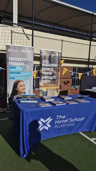 A display table for Hotel School Australia with banners, brochures, and a hotel management case study.