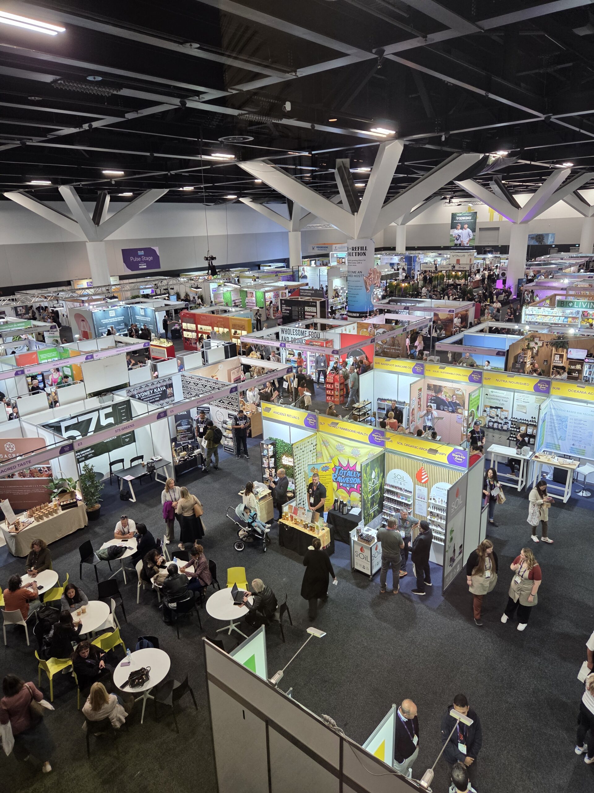 A bustling tradeshow floor with colorful booths, lively displays, and people at tables.