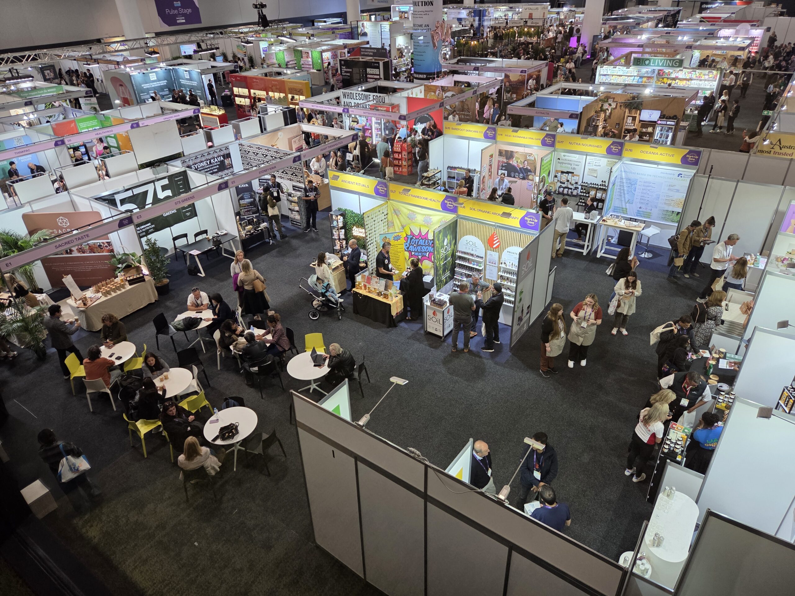 Crowded tradeshow hall with booths, displays, and people walking or sitting at tables.