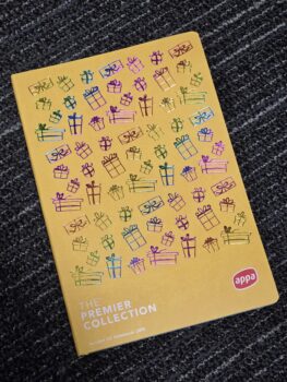 Yellow branding notebook with colorful gift box illustrations on a dark patterned carpet.