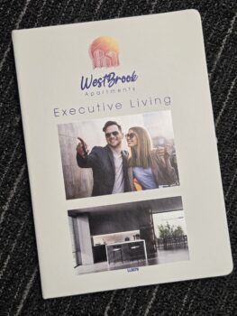 Brochure cover for WestBrook Apartments with branding notebooks, couple, and modern kitchen photos.