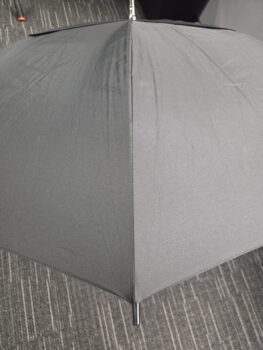 A black umbrella from a collection of umbrellas rests open on a gray, patterned carpeted floor.