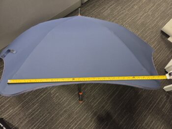 Blue fabric umbrellas on poles measured with a yellow tape, on a gray carpeted floor.