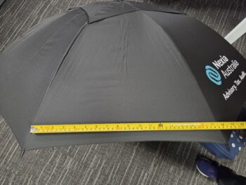 A black umbrellas with a tape measure across it, showing a width of about 90 centimeters.