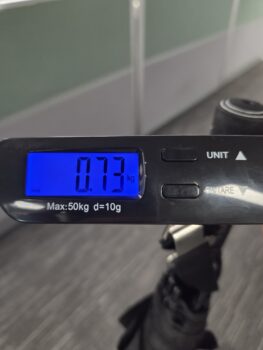 Digital scale reads 0.73 kg, with umbrellas and a suitcase handle partly visible below.