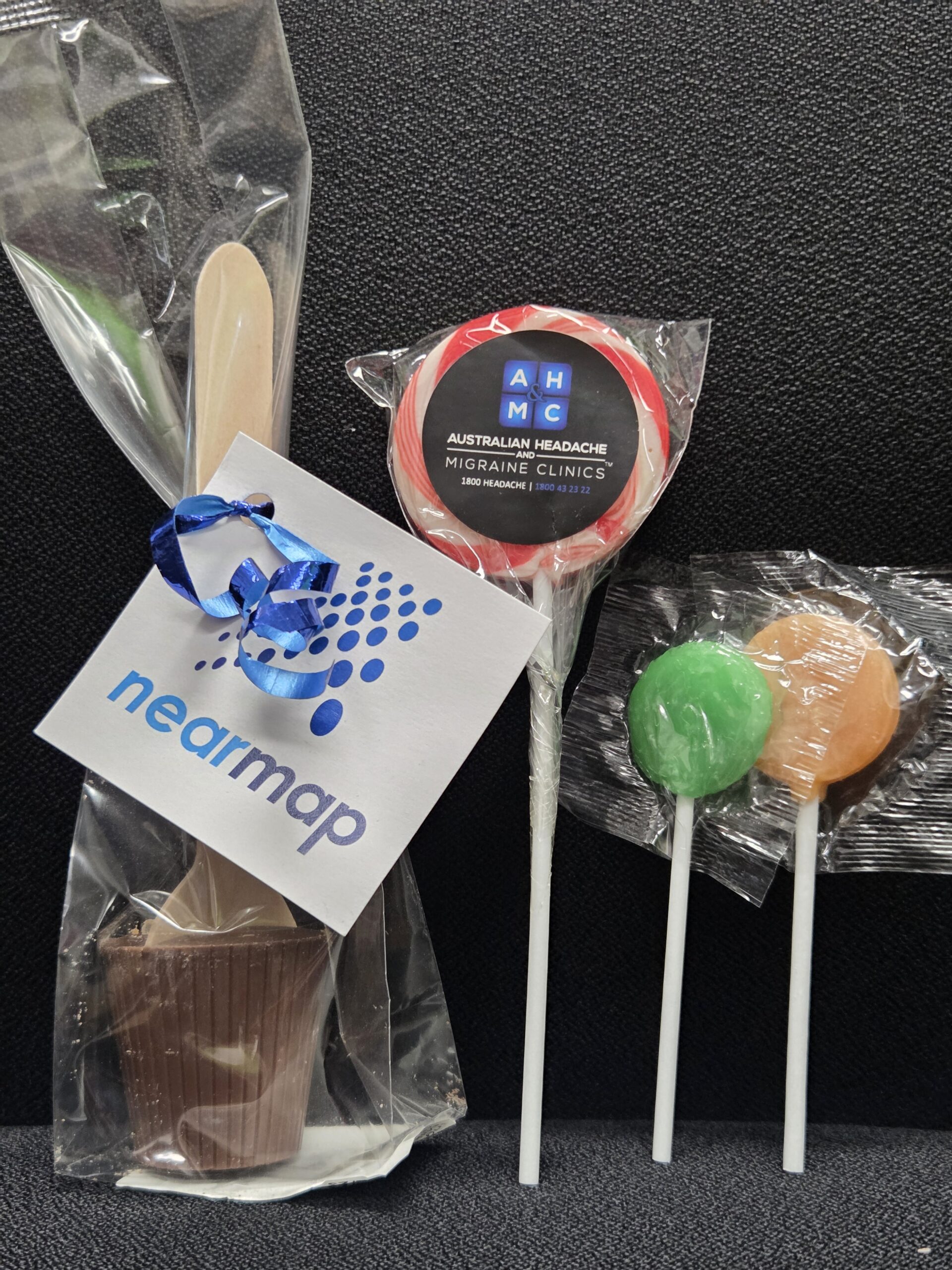 A chocolate spoon and three vibrant lollipops rest on a sleek black background.