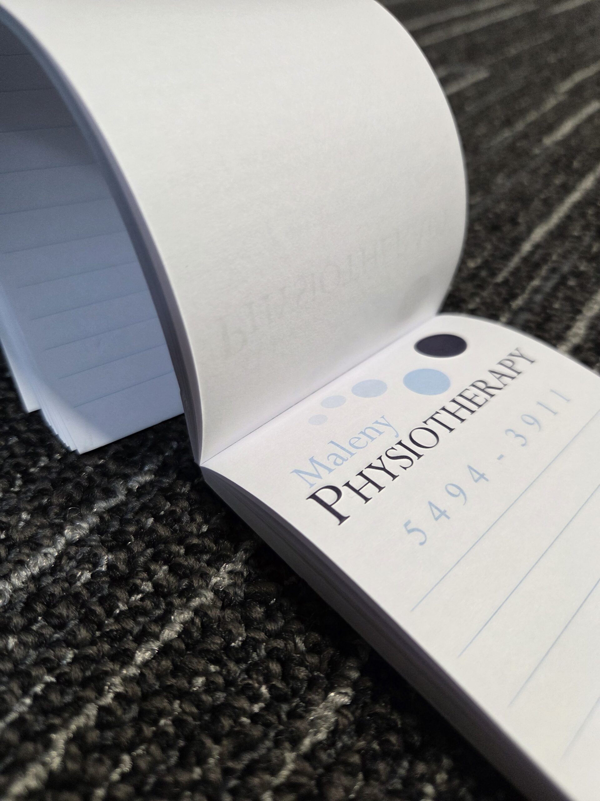 A tear-away notepad on carpet, showing Maleni PHYSIOTHERAPY and a phone number.