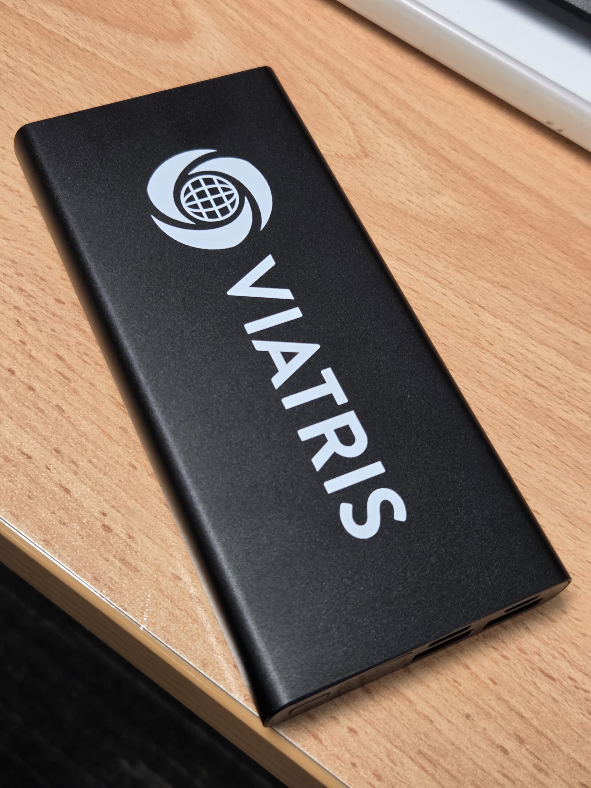 A Viatris-branded power bank sits on a wooden desk.