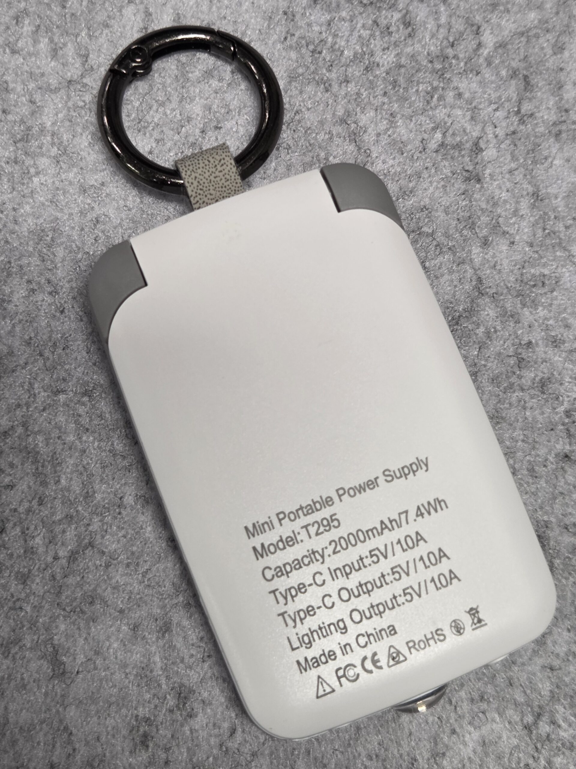 White mini portable power bank with gray corners, key ring, specs printed on back.