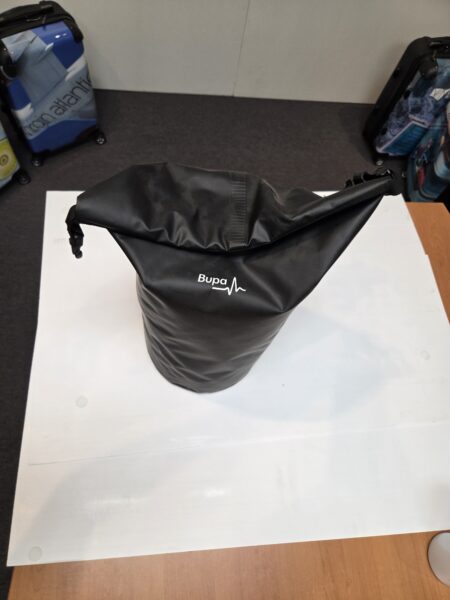 A black BUPA gym bag sits on a white sheet, with luggage in the background.
