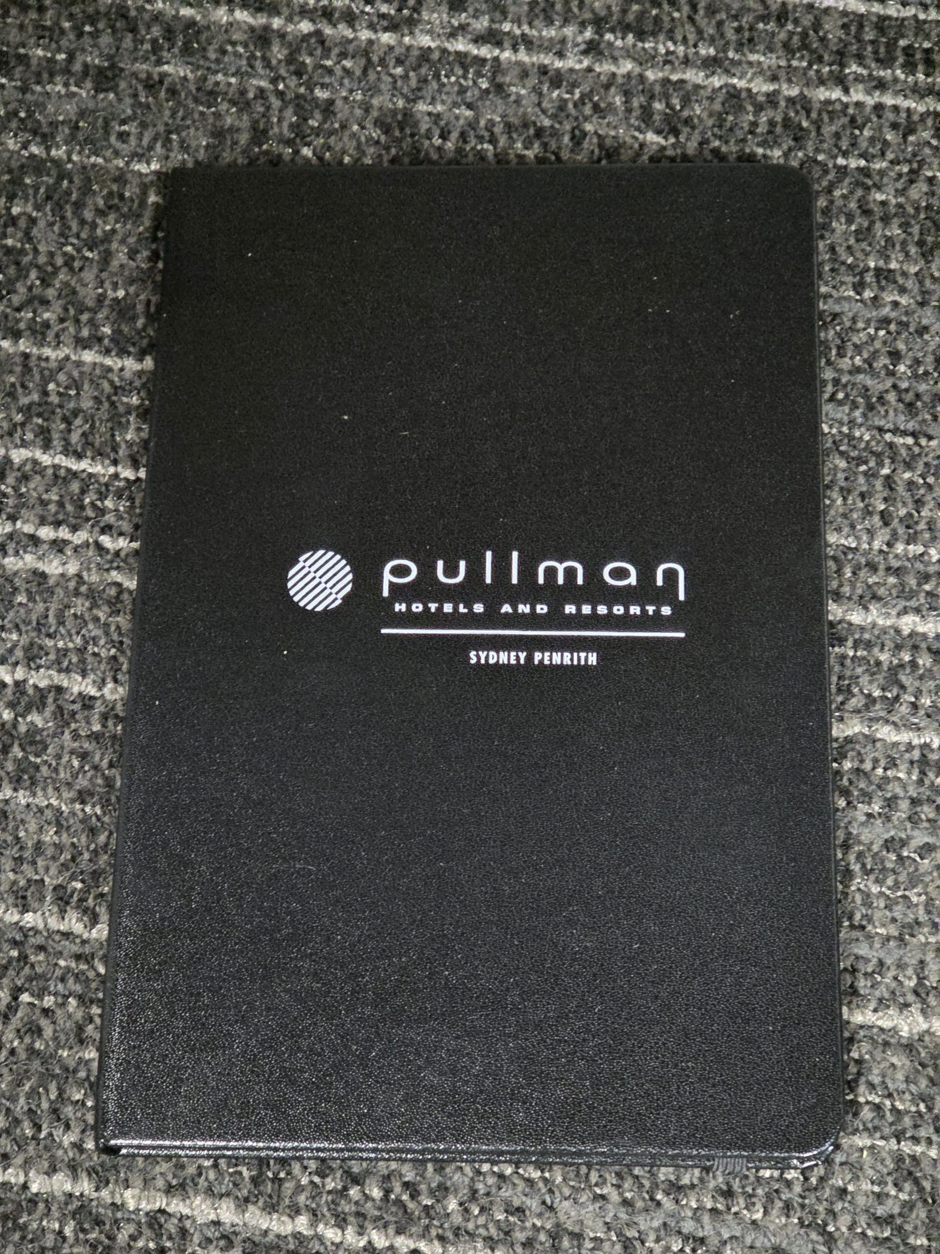 Black Pullman Hotels notebook on a grey textured carpet at Sydney Penrith Resorts.