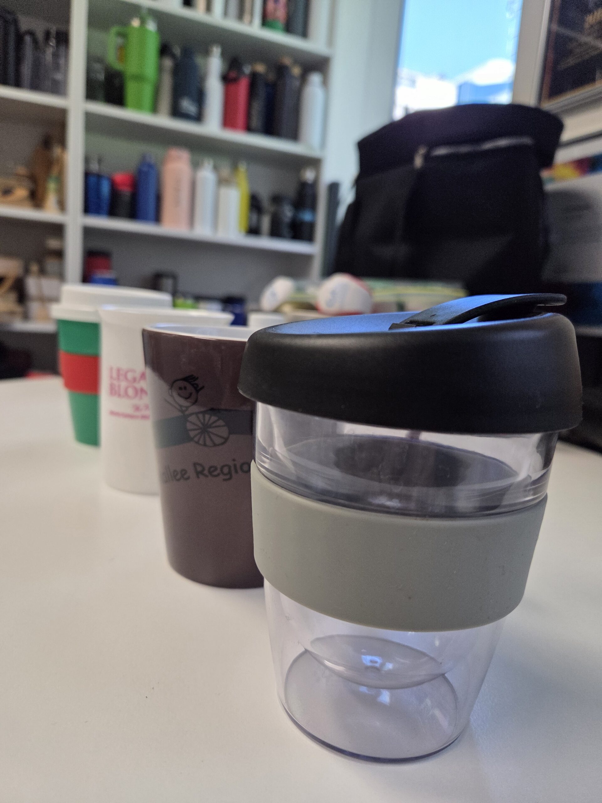 Four reusable cups on a white table, ideal for your next promotional mugs guide.