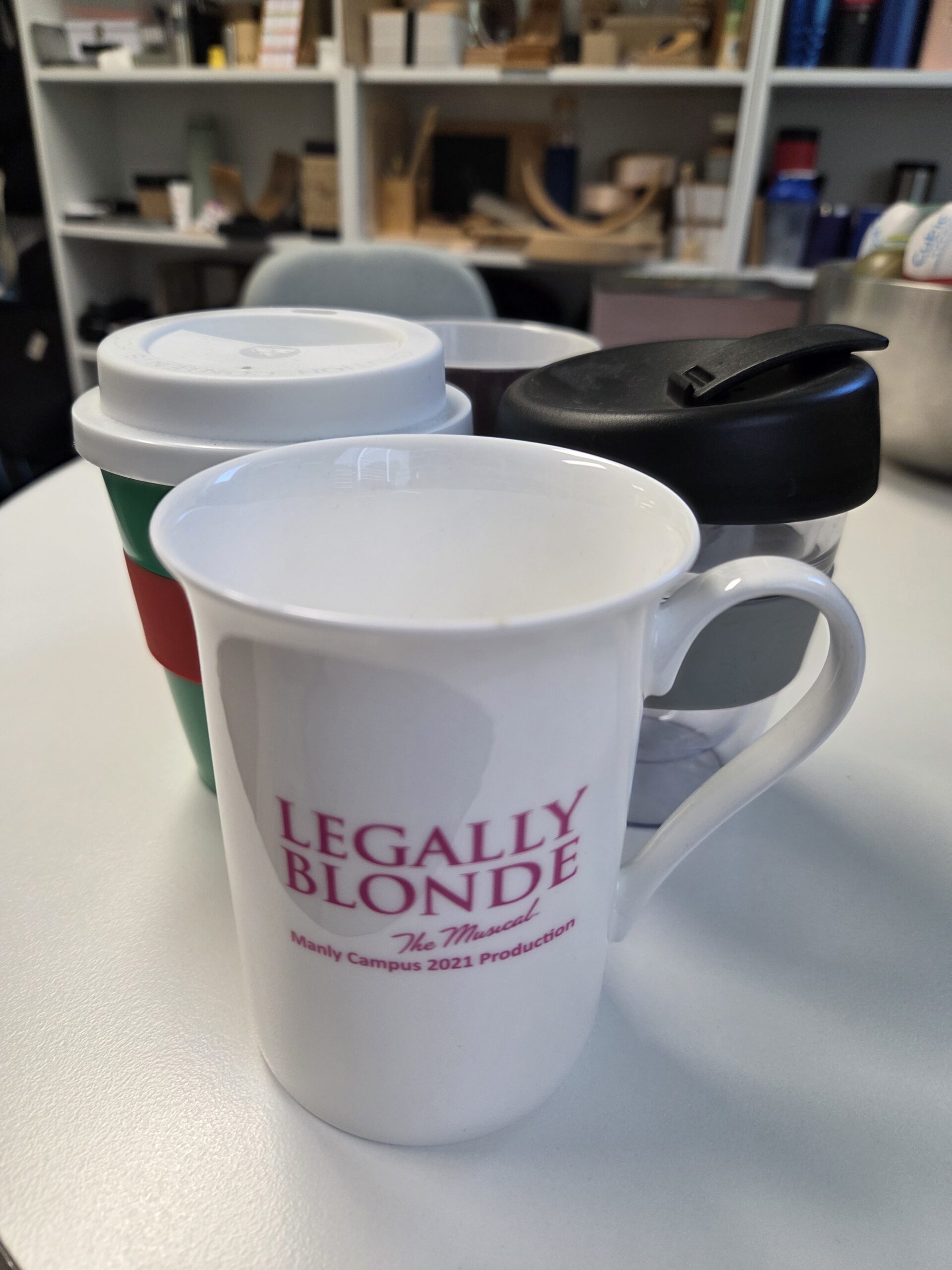 Three promotional mugs on a table, one featuring Legally Blonde The Musical.