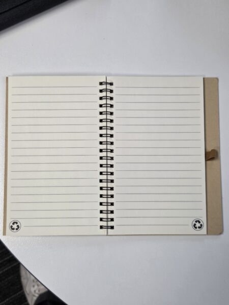 An open spiral notebook with lined pages on a white desk beside a qsuper brochure.
