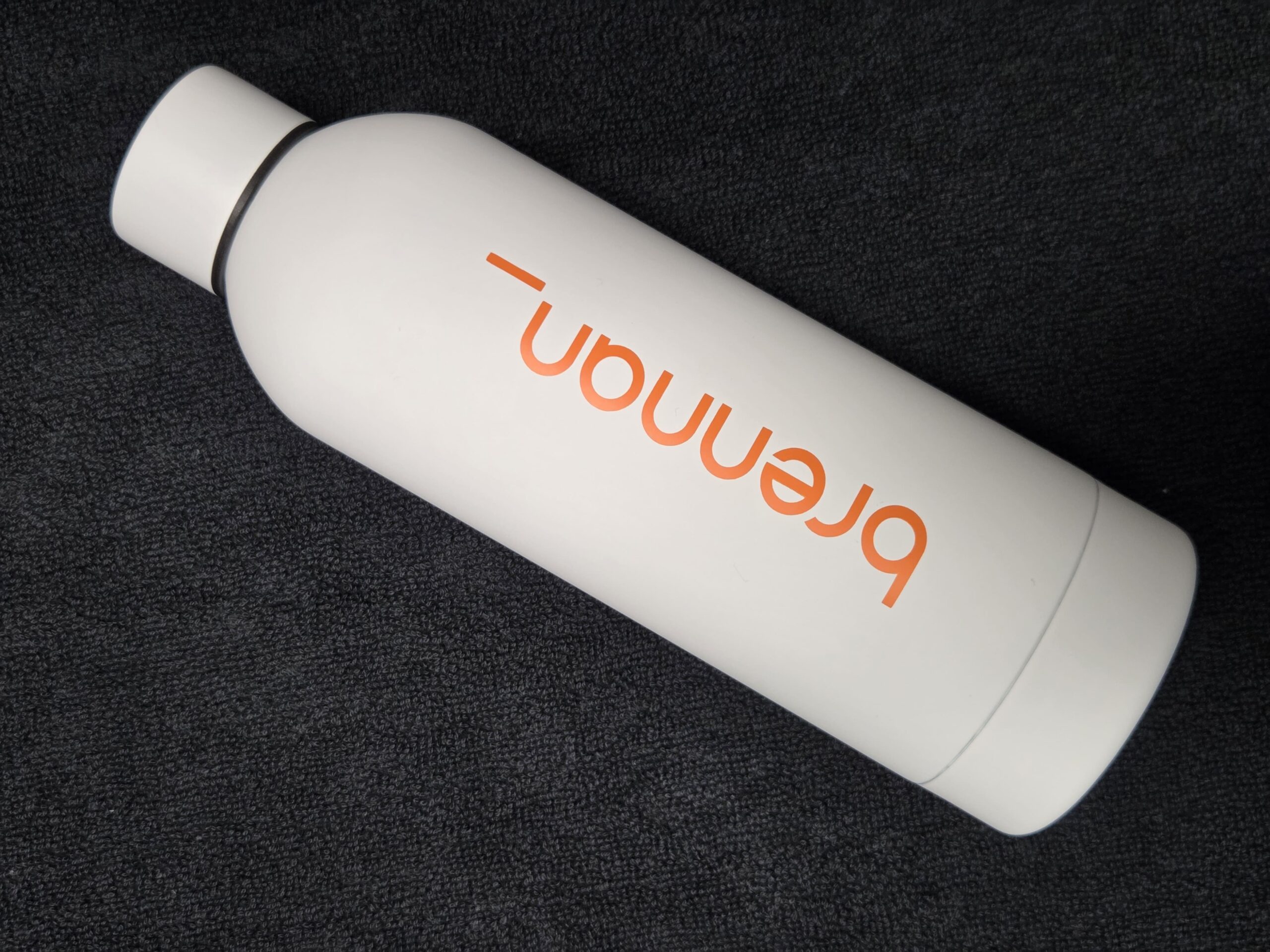 White metal bottle with orange breanon text on black textured background, perfect for tradeshows.
