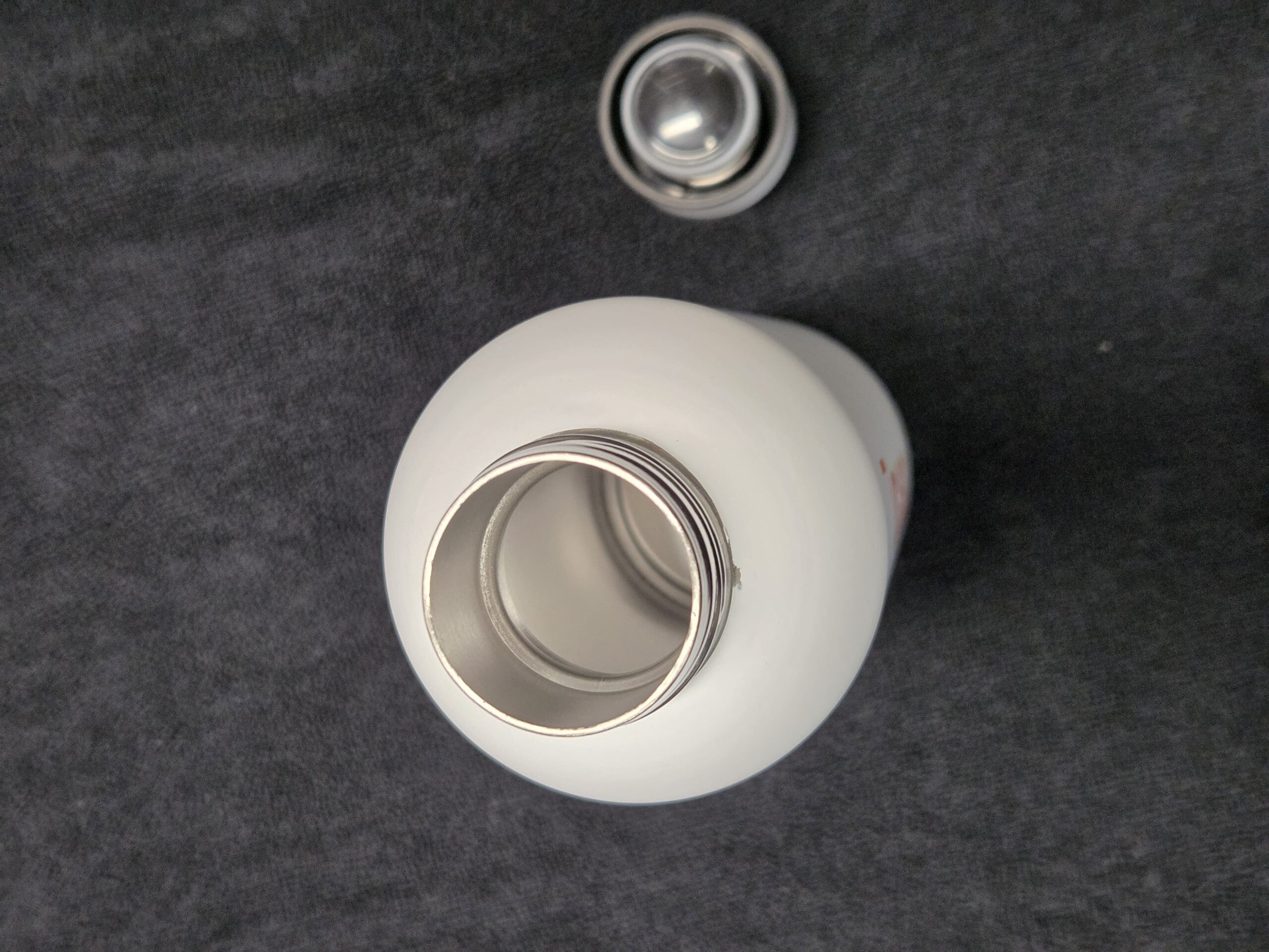 Open white metal bottle with lid above it on a dark gray surface, perfect for tradeshows.