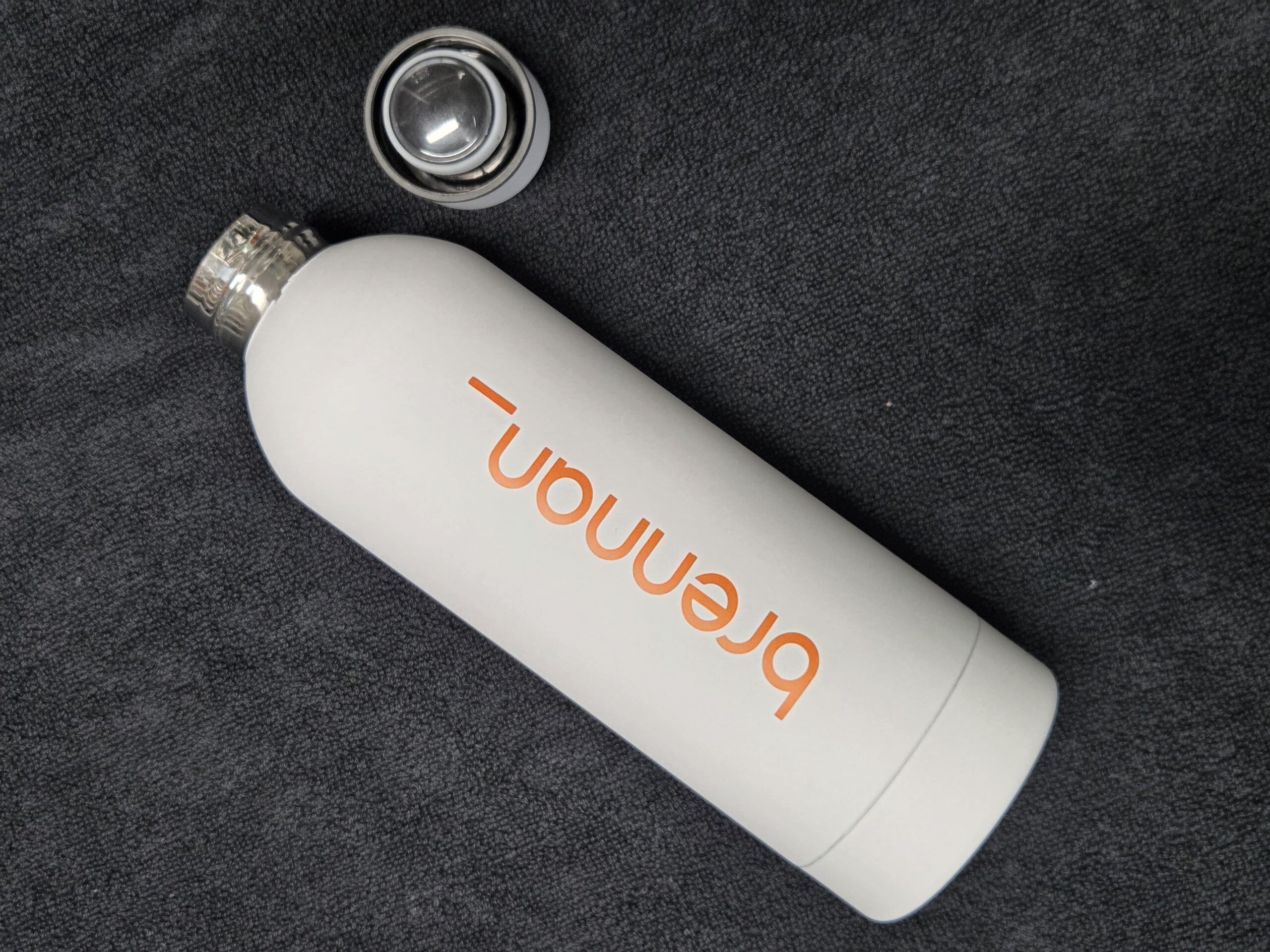 White metal bottle with Breman text, cap nearby—perfect for tradeshow giveaways.
