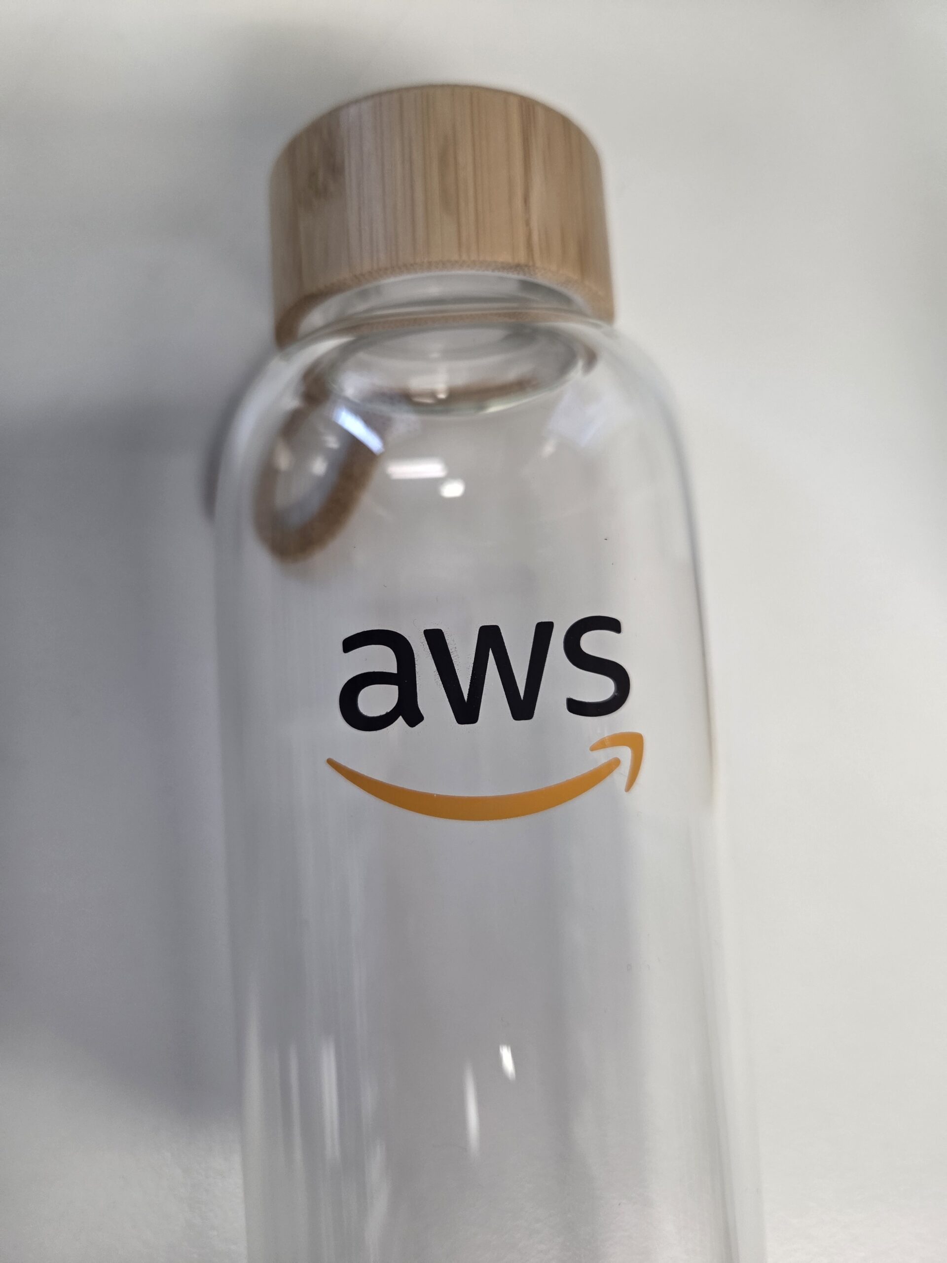 Clear AWS Branded Glass drink bottle with bamboo lid, featuring the AWS logo and orange smile.