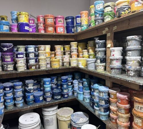 Shelves filled with colorful paint containers, organized by shade, labeled for print setup fees.