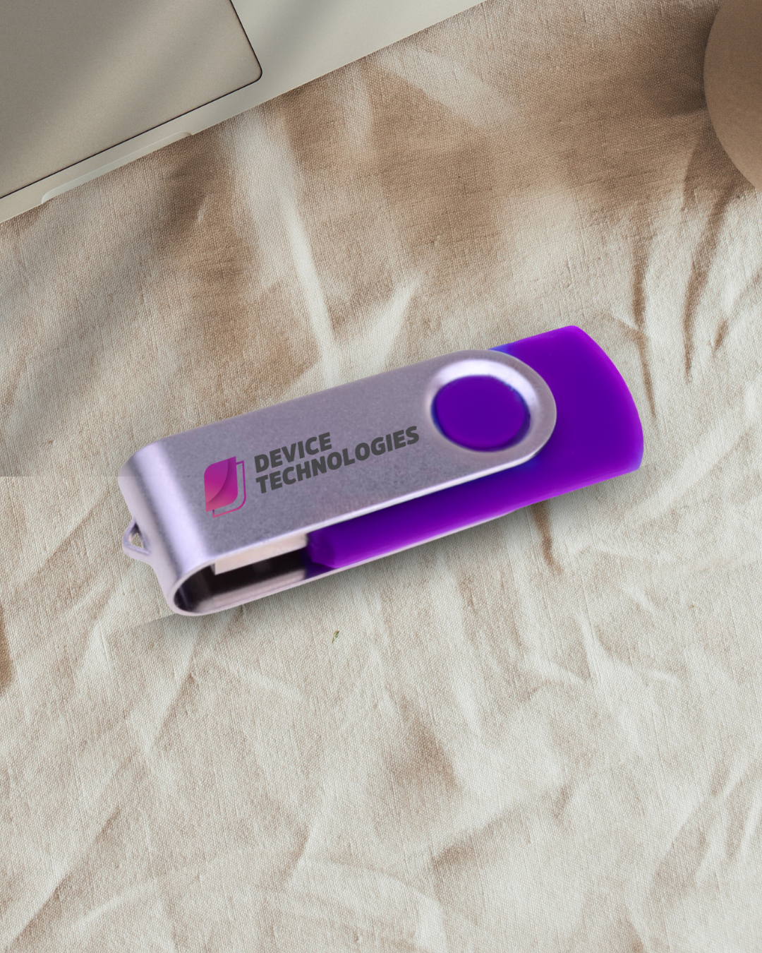 A purple and silver USB flash drive from medical devices supplier Device Technologies on beige fabric.