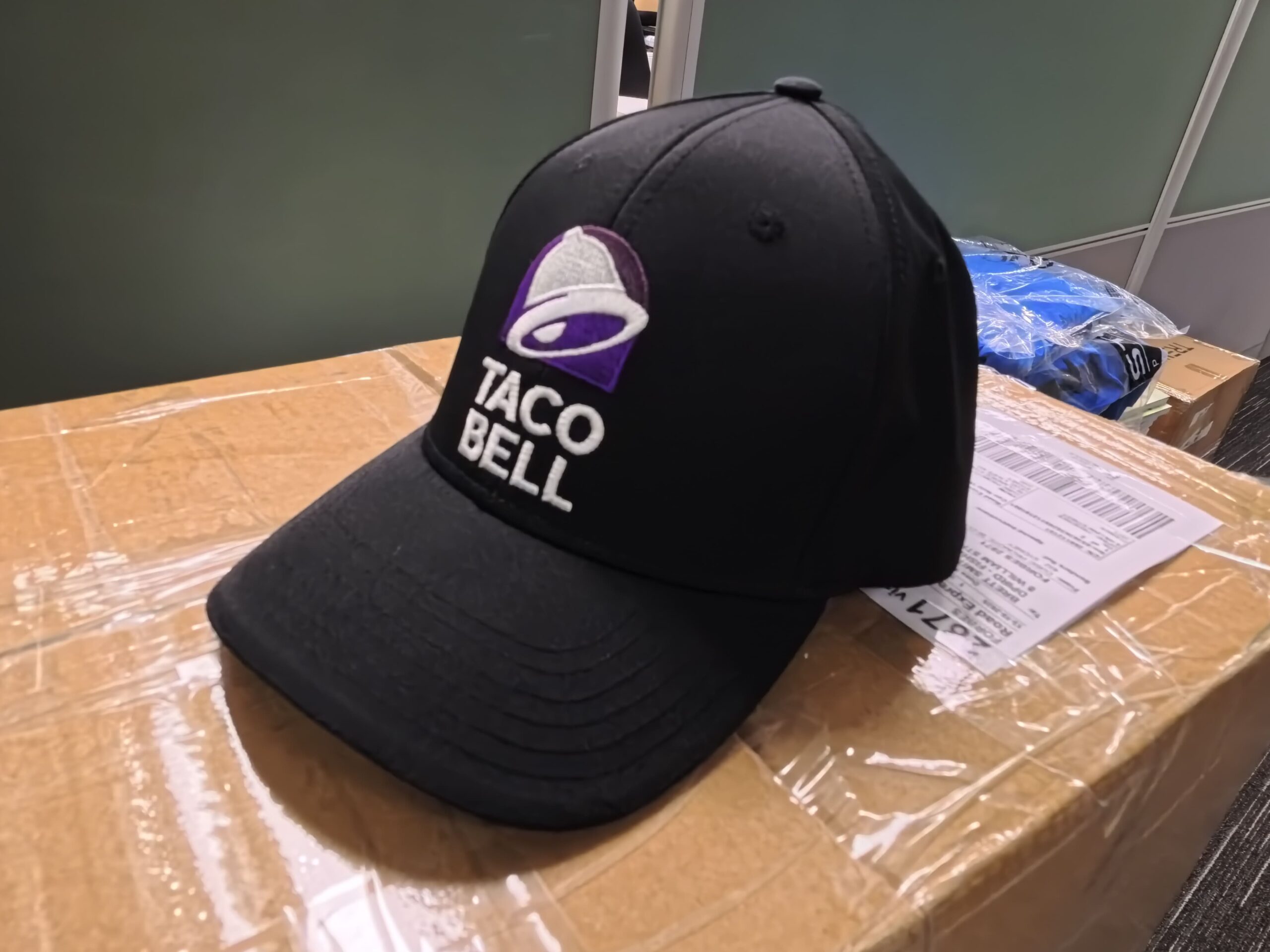 A black Taco Bell cap rests on a taped cardboard box, shipped to Australia.