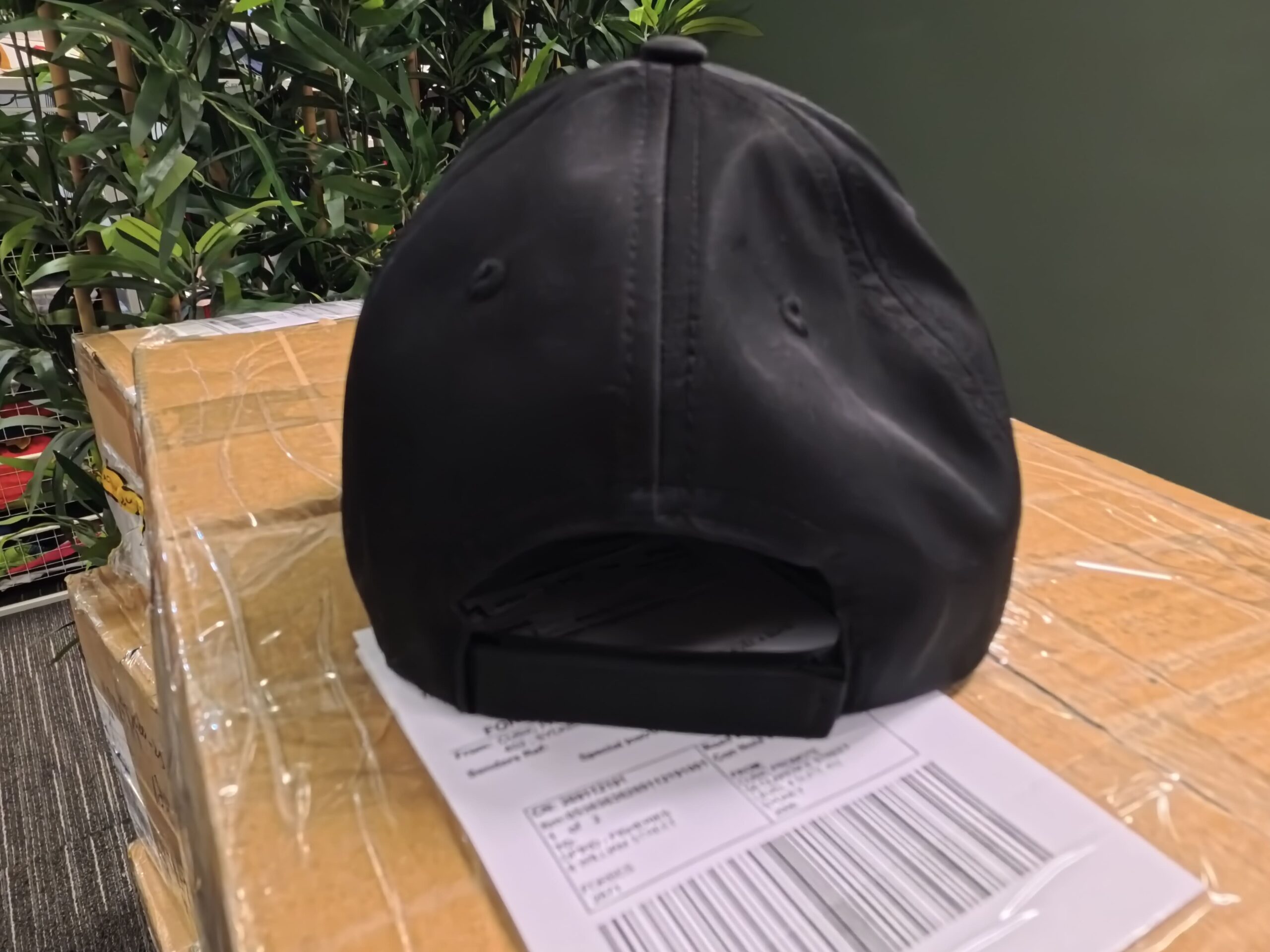 A black Taco Bell cap rests on a box with shipping labels, near green plants in Australia.
