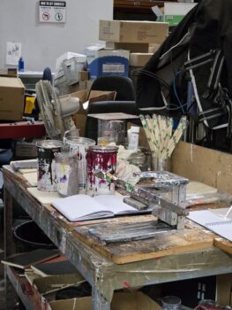 Messy art studio table with paint cans, brushes, and a notice about Print Setup Fees scattered around.