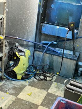 A pressure washer and tangled hose sit beside print setup fees in a messy, blue-stained room.