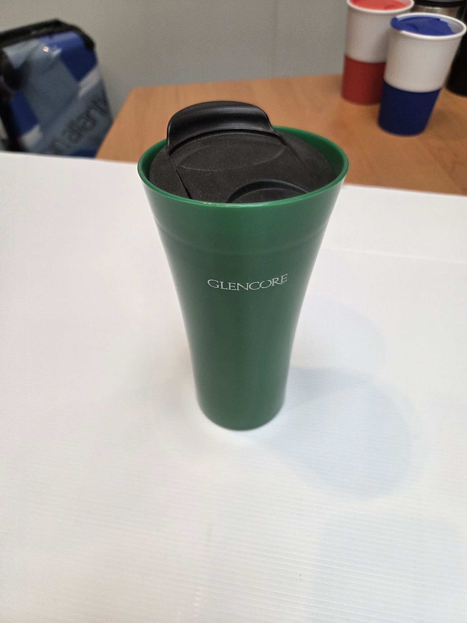 Green Glencore travel mug on a white table, perfect for sharing your client story over coffee.