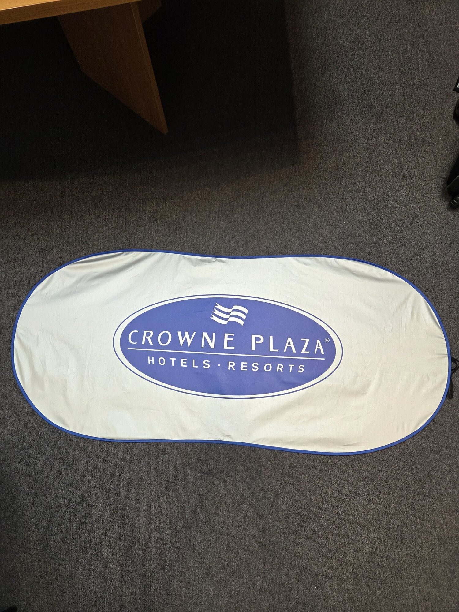 Oval Crowne Plaza hotels logo sign resting on a gray carpeted floor.