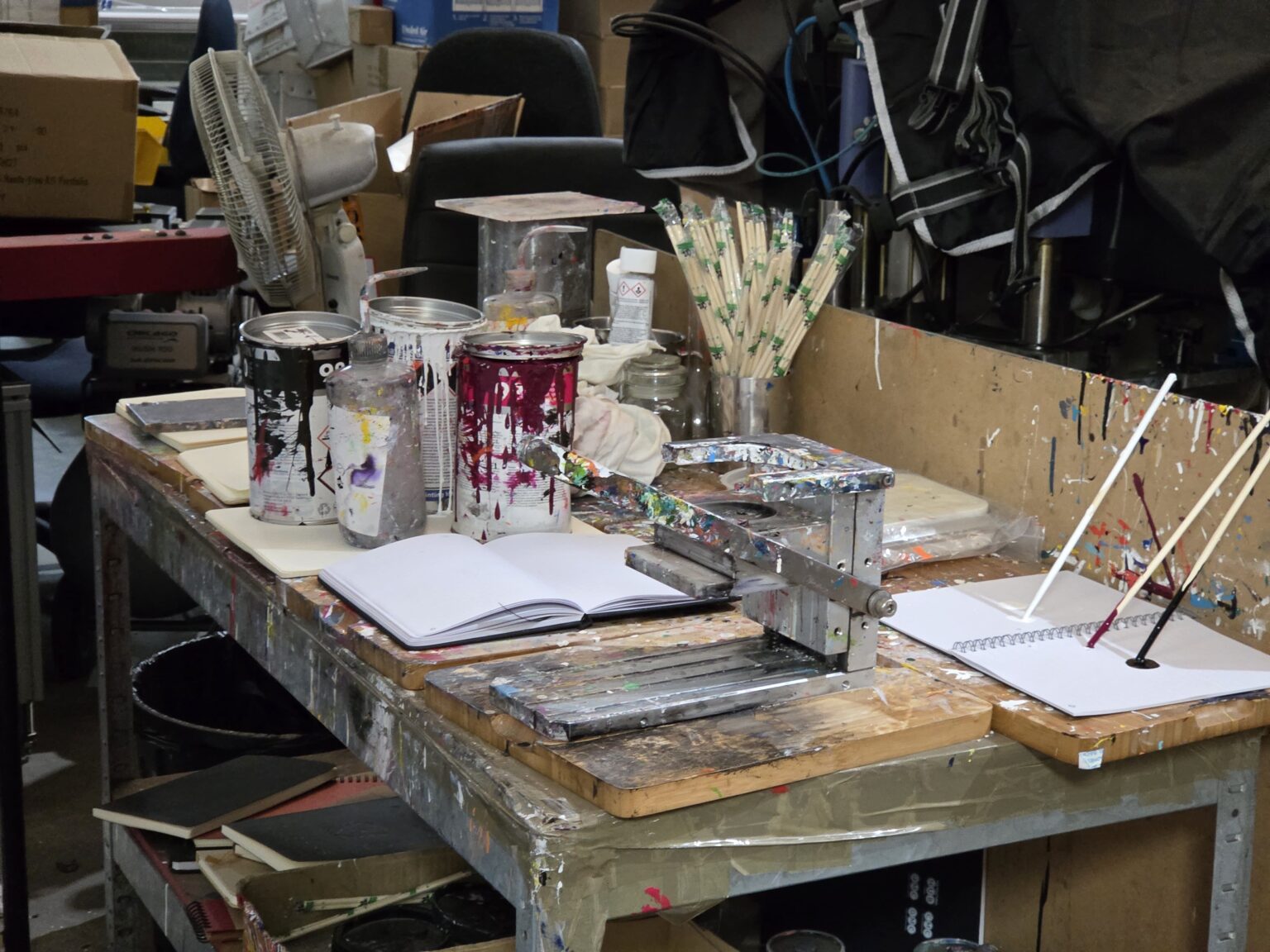 A messy art studio table, scattered with supplies and paint cans, hints at rush orders in progress.
