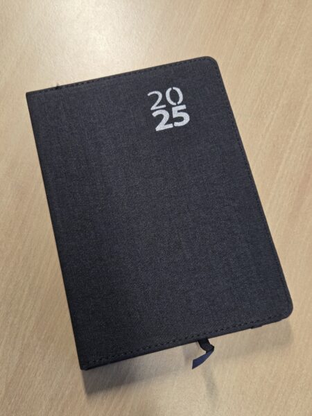 A black 2025 planner lies closed on a light wood surface, perfect for Christmas gifts.