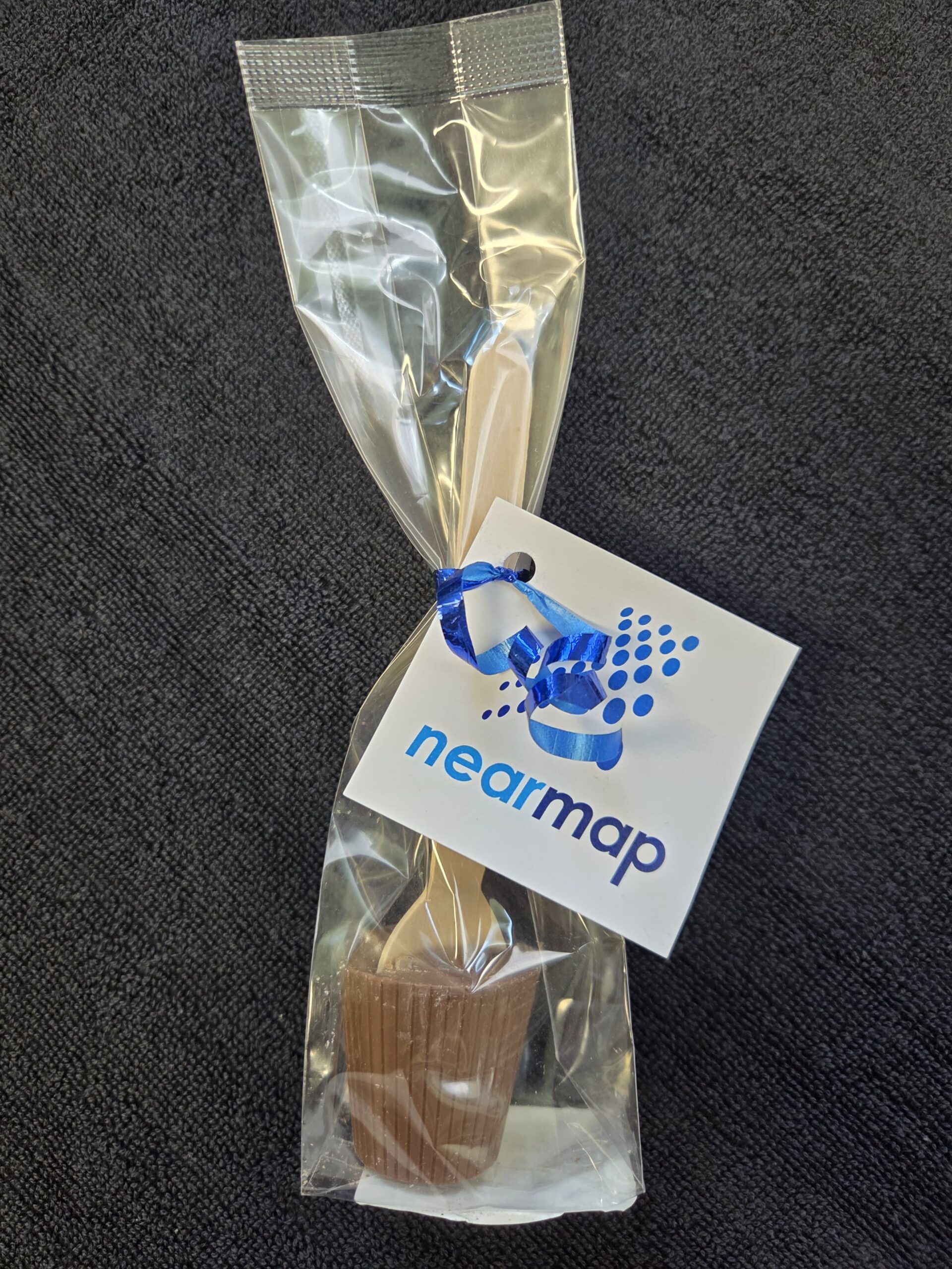 Chocolate treat on a stick, wrapped in plastic with a Nearmap tag and blue ribbon—sweet Client Story!.