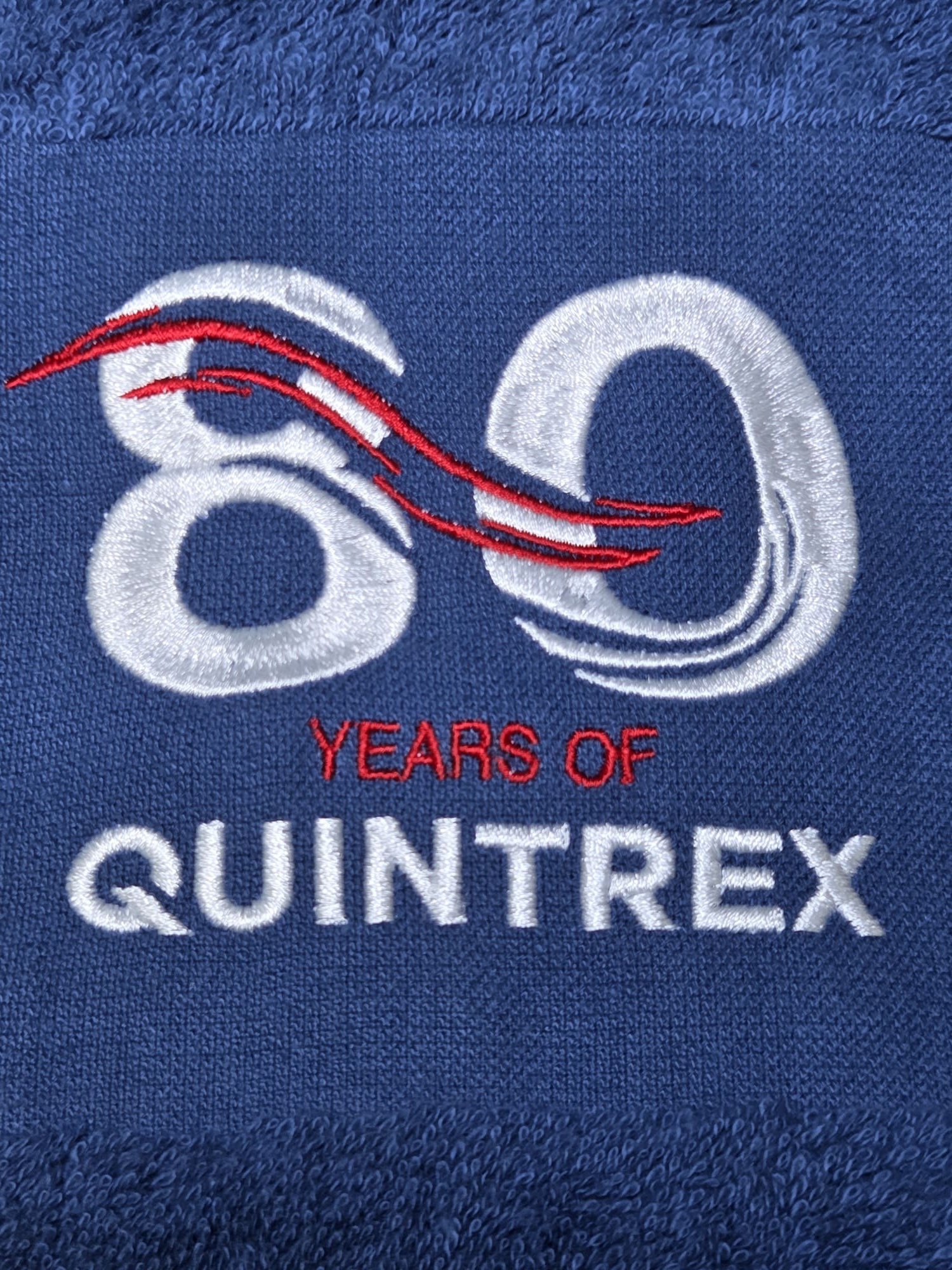 Blue fabric with Quintrex 80 Years embroidered in white and red thread.