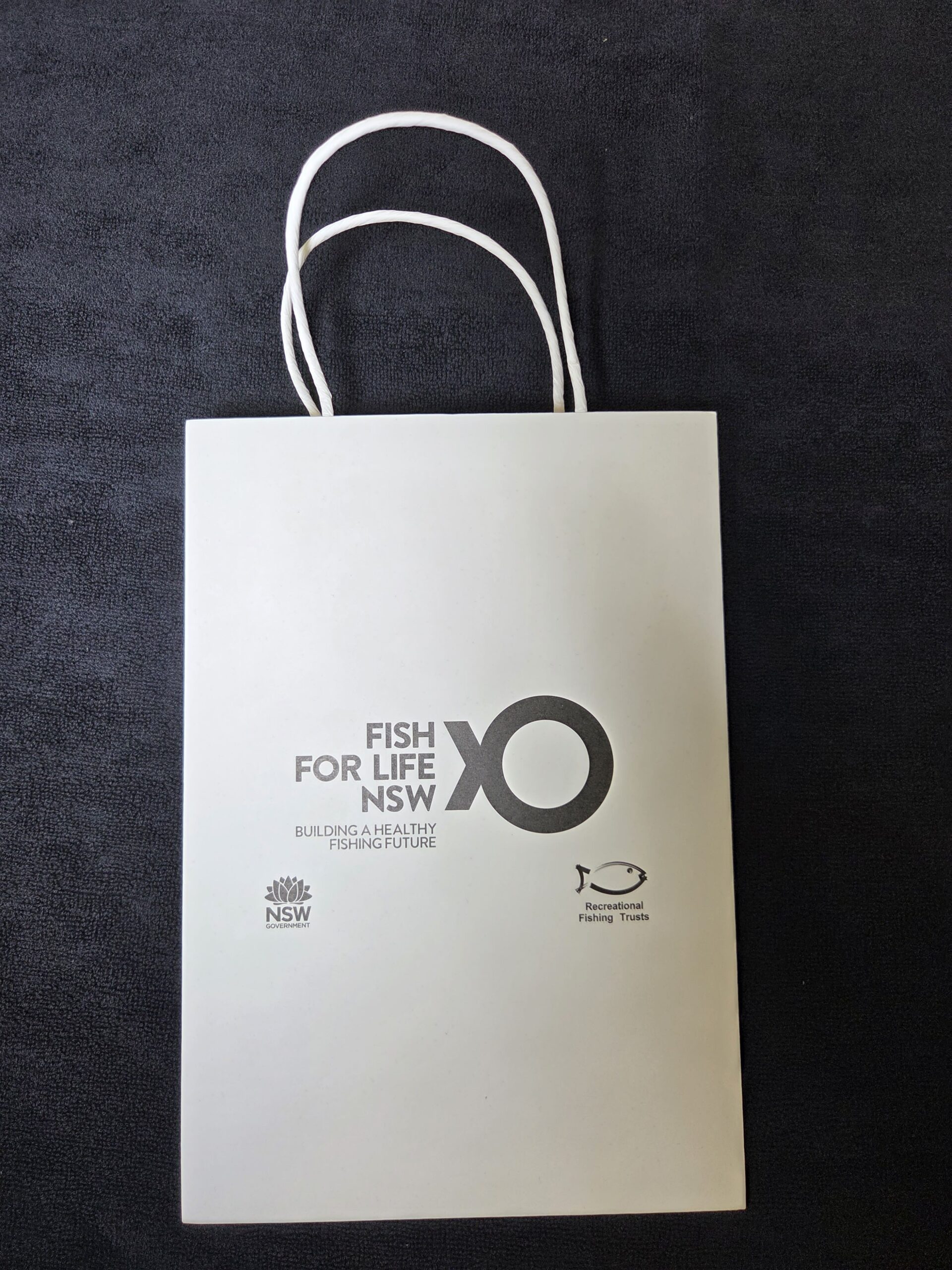 White gift bag featuring Fish for Life and NSW Government logos on a dark background.